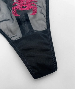 Macro detail of intricate pink scorpion embroidery on sheer black mesh lingerie fabric