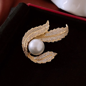 Vue macro d'une broche feuille dorée avec perle blanche et zircon dans un écrin à bijoux