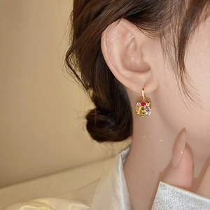 Close-up of elegant gold earrings with multi-color square gemstones worn by a model