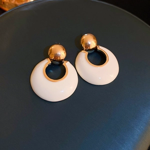 Close-up of French-style gold circle earrings with cream resin on blue leather background