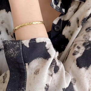 Detailed view of a twisted gold rope bracelet on a wrist with black and white texture