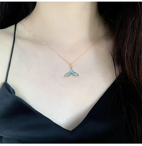 Nahaufnahme einer feinen Goldkette mit einem blauen Walflossen-Emaille-Anhänger am Hals