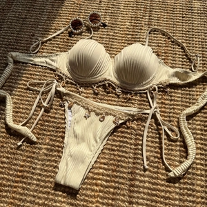 Close-up of cream ribbed bikini with 3D shell cups and hanging starfish charms on straw mat