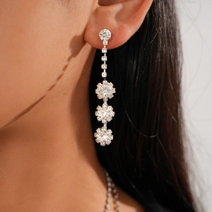 Close-up of dangling silver flower earrings with crystals on a model's ear