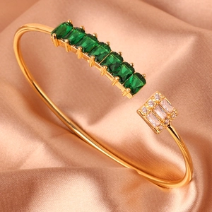 Detailopname van gouden open armband met smaragdstenen op luxe champagne zijden achtergrond