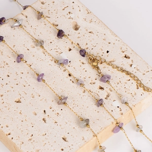 Gold stainless steel chain necklace with purple and grey natural stone beads on travertine