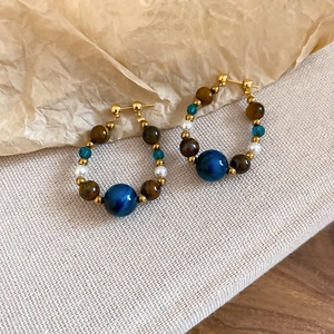 Detailed shot of retro tiger eye and pearl beaded earrings on linen fabric background