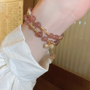 Detail of pink strawberry quartz double-layer bracelet with gold bow charm and faceted beads