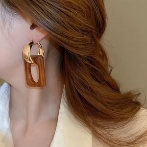 Close-up of geometric resin drop earrings in amber gold on a model with elegant styling