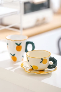 Detail of hand-painted orange ceramic coffee cup and saucer set with green handle