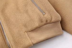 Detailed close-up of camel wool-like jacket featuring silver zipper and ribbed cuffs