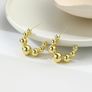 Detailed close-up of 18k gold plated hollow ball C-shaped stud earrings on ceramic tray