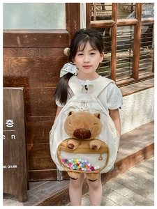 Detail view of cream canvas children backpack with 3D Capybara plush and colorful pom-poms