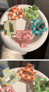 Close-up of square acrylic hair claws with colorful checkerboard pattern on a white plate
