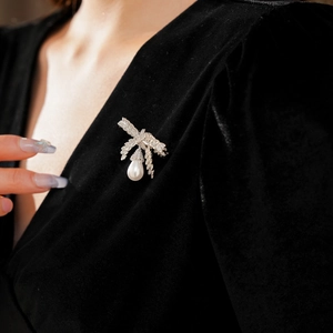 Détail macro d'une broche nœud en argent et perle avec zircons sur velours noir