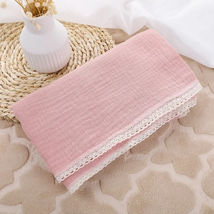 Detail of pink cotton baby swaddle with white lace edge on a soft textured fabric