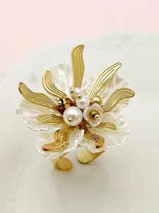 Close-up of golden floral ring with white pleated petals and pearl center on porcelain
