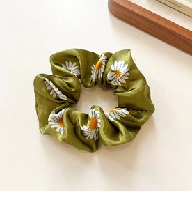 Close-up of olive green daisy pattern silk scrunchie with elastic pleated texture