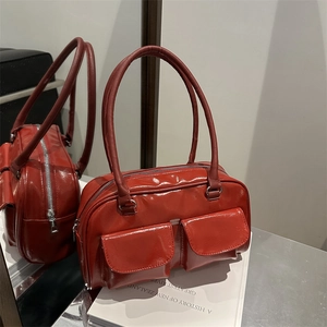 Elegante borsa sottobraccio rossa in ecopelle con tasche frontali sopra un libro bianco