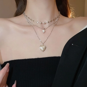 Close-up of triple-layer necklace featuring pearl charms and embossed heart pendant