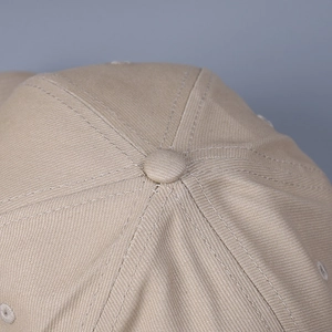Detail of the cotton twill top button and stitching on a beige structured baseball cap