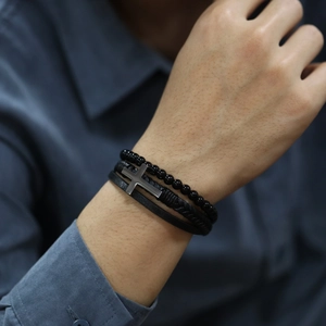 Detail of multi-layer black leather bracelet set with cross charm and beads on wrist