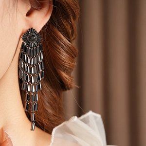 Close-up of black geometric zircon tassel earrings worn by a model in soft lighting
