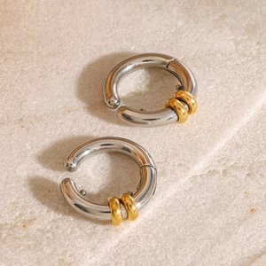 Minimalist silver and gold two-tone stainless steel ear cuff earrings on stone background