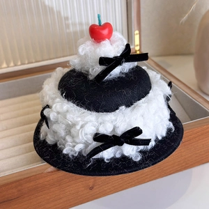Detail of a plush cake hair clip featuring a red cherry, black bows, and soft lamb wool