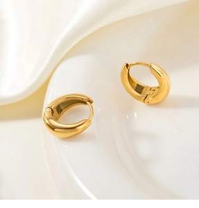 Detailed view of chunky gold drop huggie earrings on white silk and ceramic plate