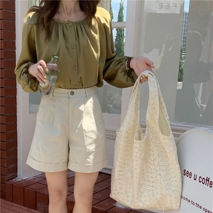 Close-up of white floral lace cutout canvas tote bag styled with olive green shirt