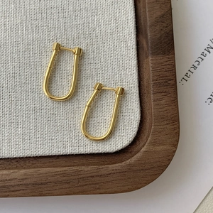 Macro shot of minimalist gold U-shaped hoop earrings on elegant fabric background