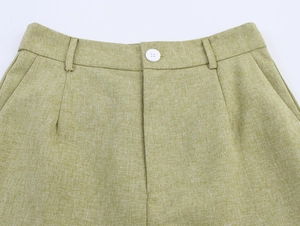 Detail of light green linen pants featuring a white button, belt loops, and pleated waist