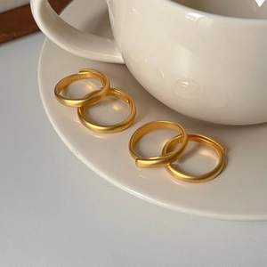 Minimalist matte gold rings displayed on white ceramic saucer in natural sunlight