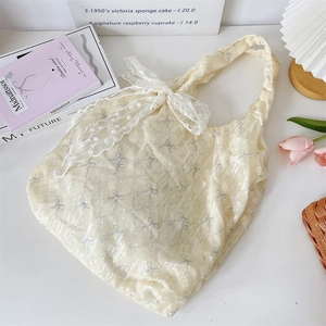 Détail du sac fourre-tout beige avec imprimés nœuds bleus et nœuds en dentelle blanche