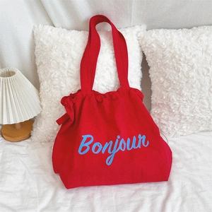 Detail of red canvas tote bag with blue Bonjour print against a white cushion and lamp