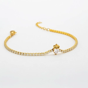 Detail of gold tennis bracelet with heart zircon and crown pendant on white background