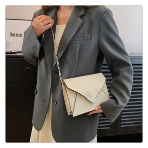 Detail of off-white envelope crossbody bag with V-shaped metal buckle and chain strap