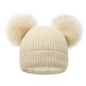 Detail of beige knitted winter hat featuring dual faux fur pom-poms and warm fleece lining