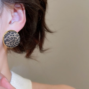 Detailed view of round leopard print earrings with gold trim worn by a model