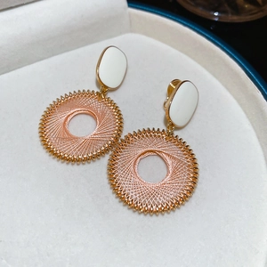 Dettaglio degli orecchini a cerchio in metallo dorato intrecciato con smalto bianco elegante