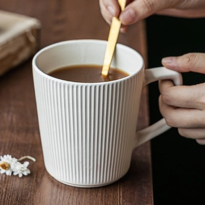 Japanese style white ceramic mug with vertical ribbed texture and gold spoon on wood table
