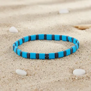 Detail of bohemian sky blue and charcoal grey square bead bracelet on a sandy beach background