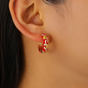 Close-up of a model wearing red enamel floral hoop earrings with retro gold accents