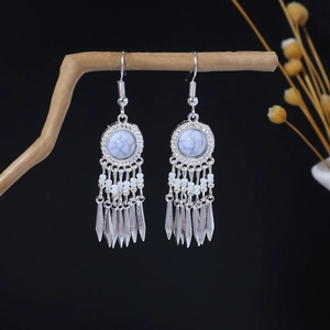 Detail of silver bohemian earrings with white stone and tassel on a dry branch