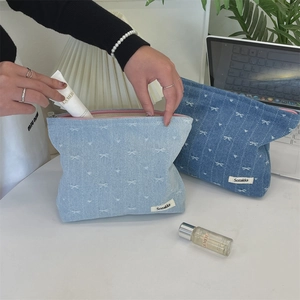 Detail of denim cosmetic bag with white bow embroidery and pink zipper closure