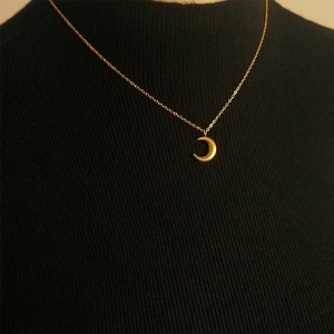 Minimalist gold moon pendant necklace in titanium steel on a black knit background