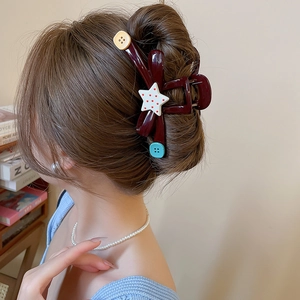 Detail of dark red acrylic star hair claw clip with colorful button accents on a model