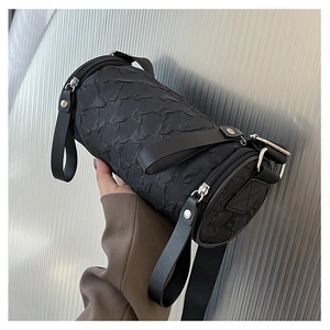 Close-up of black cylinder crossbody bag showing textured fabric and silver hardware