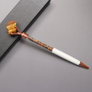 Macro view of white metal ballpoint pen featuring Tiger Eye stones and rose gold metal